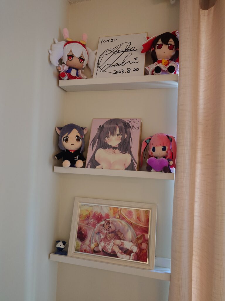 A few display shelves with shikishis, a pub frame, and plushies.